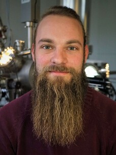 Herr Leisegang mit langer Bartfrisur, sitzt in einem Labor oder technischen Umfeld.